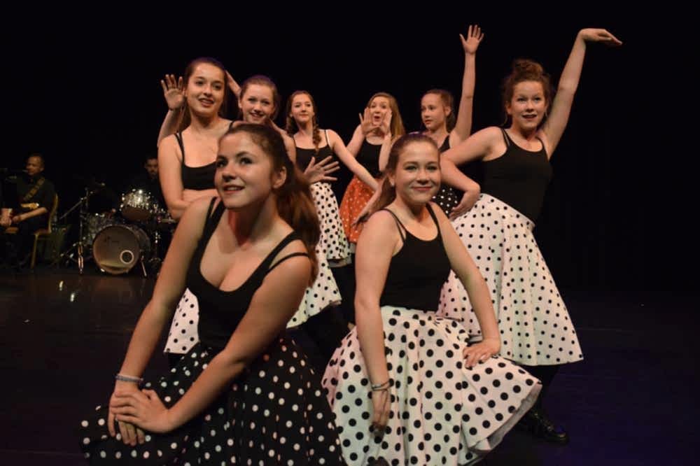 groep meisjes met gestippelde rokken zwart-wit zit en danst op een lied op het podium